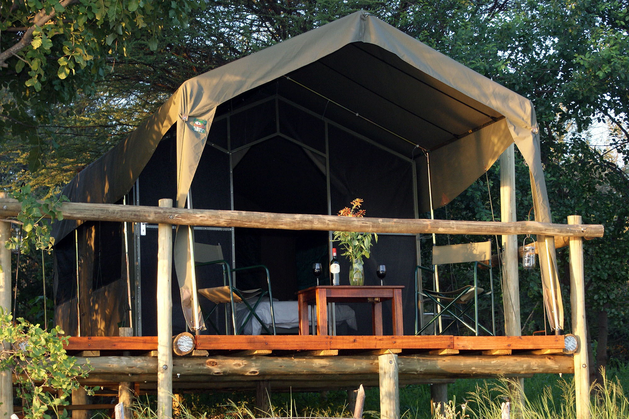 Komfortable Safari-Zeltlodge auf einer erhöhten Holzplattform in Botswana, umgeben von dichter Vegetation. Die naturnahe Unterkunft verfügt über eine private Veranda mit Sitzgelegenheiten und bietet ein authentisches Safari-Erlebnis in der afrikanischen W