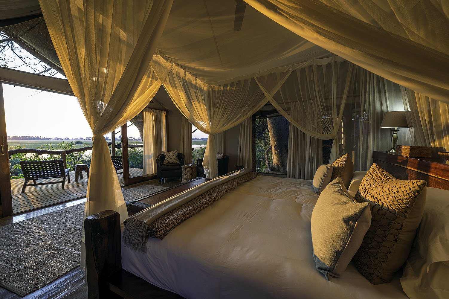 Elegante Safari-Suite mit Himmelbett, Moskitonetz und Terrasse mit Blick auf die Wasserlandschaft des Okavango-Deltas in Botswana.