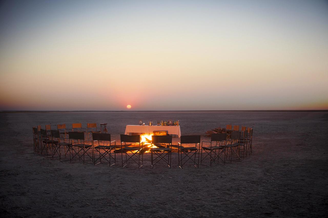 Exklusives Abendessen am Lagerfeuer in den Makgadikgadi-Salzpfannen in Botswana bei Sonnenuntergang, umgeben von der Weite einer der größten Salzflächen der Erde.