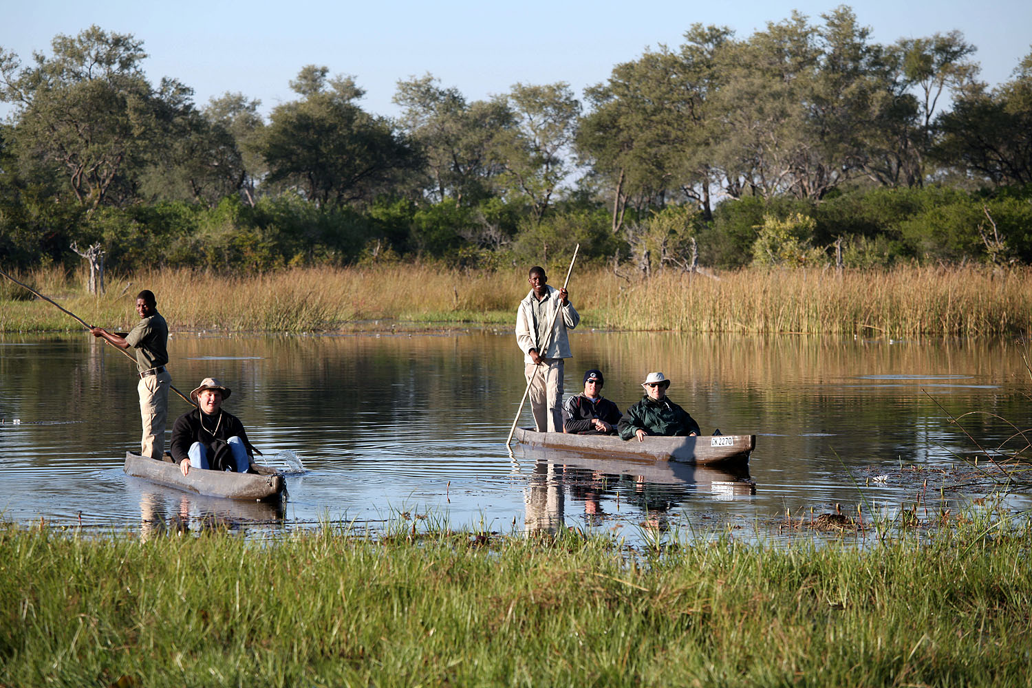 Gäste gleiten in traditionellen Mokoro-Einbäumen durch die Wasserwege des Okavango-Deltas in Botswana, begleitet von erfahrenen Guides.