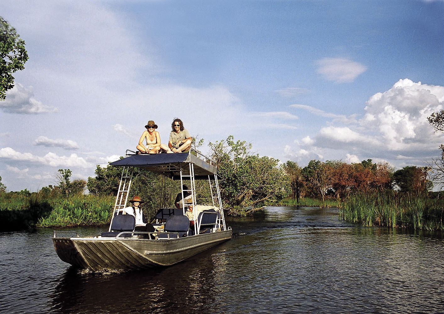 Reisende auf einer Bootssafari im Okavango-Delta in Botswana. Das Safari-Boot gleitet durch die schmalen Wasserwege des Deltas und ermöglicht intensive Natur- und Tierbeobachtungen in einer der artenreichsten Regionen Afrikas.