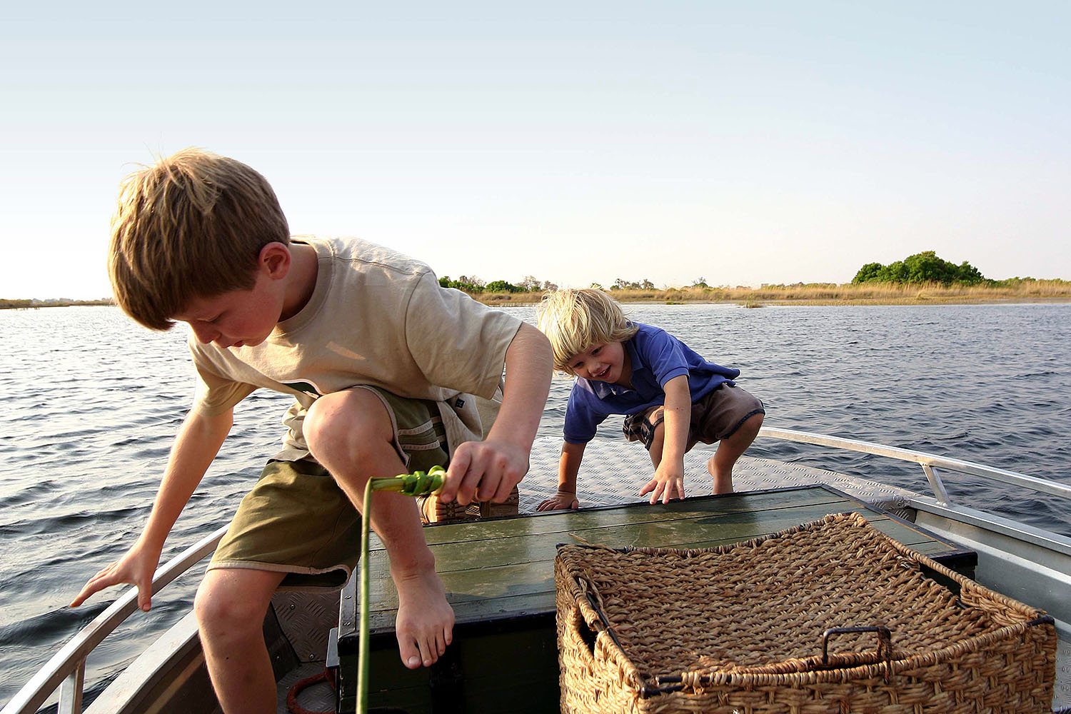 Zwei Kinder erkunden während eines Bootsausflugs das Okavango-Delta in Botswana. Die Szene zeigt ein familienfreundliches Safari-Erlebnis auf den Wasserwegen des Deltas und vermittelt Abenteuer, Naturverbundenheit und Entdeckergeist in der afrikanischen W