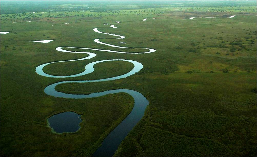 Luftaufnahme des Okavango-Deltas in Botswana mit einem sich durch die weite Landschaft schlängelnden Wasserlauf. Das einzigartige Binnendelta zählt zu den größten Naturwundern Afrikas und ist ein bedeutendes Safari- und Wildnisgebiet in Botswana.