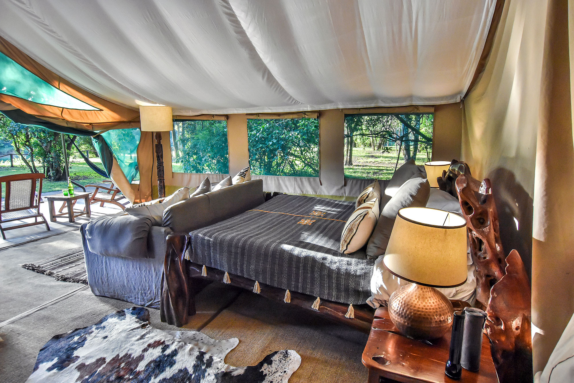 Stilvoll eingerichtetes Safari-Zelt mit großem Bett, gemütlicher Sitzecke und Blick in die afrikanische Natur.