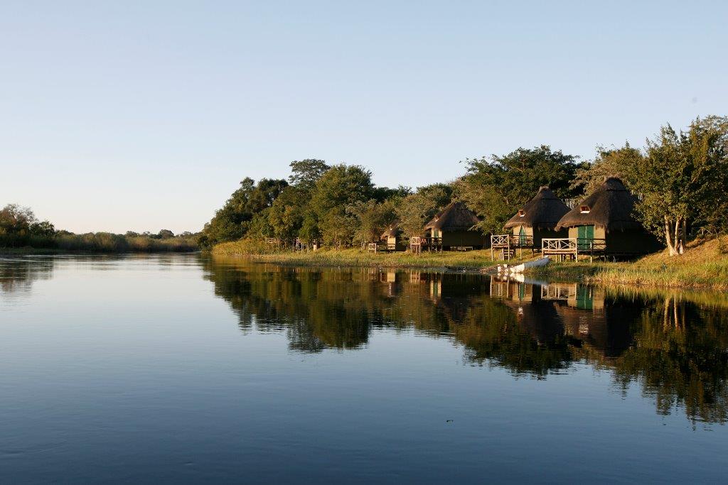Safari-Lodge mit traditionellen Chalets am ruhigen Ufer des Okavango-Flusses in Namibia.