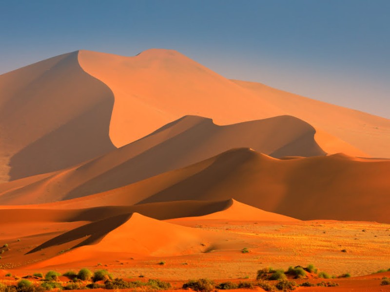 Leuchtend rote Sanddünen der Namib-Wüste in Namibia im warmen Morgen- oder Abendlicht.