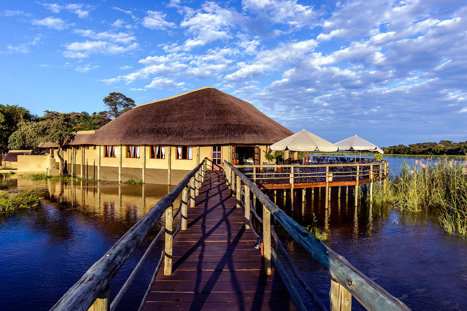 Komfortable Safari-Lodge auf Stelzen am Wasserufer des Chobe-Flusses mit Holzsteg und Sonnenterrasse in Botswana.