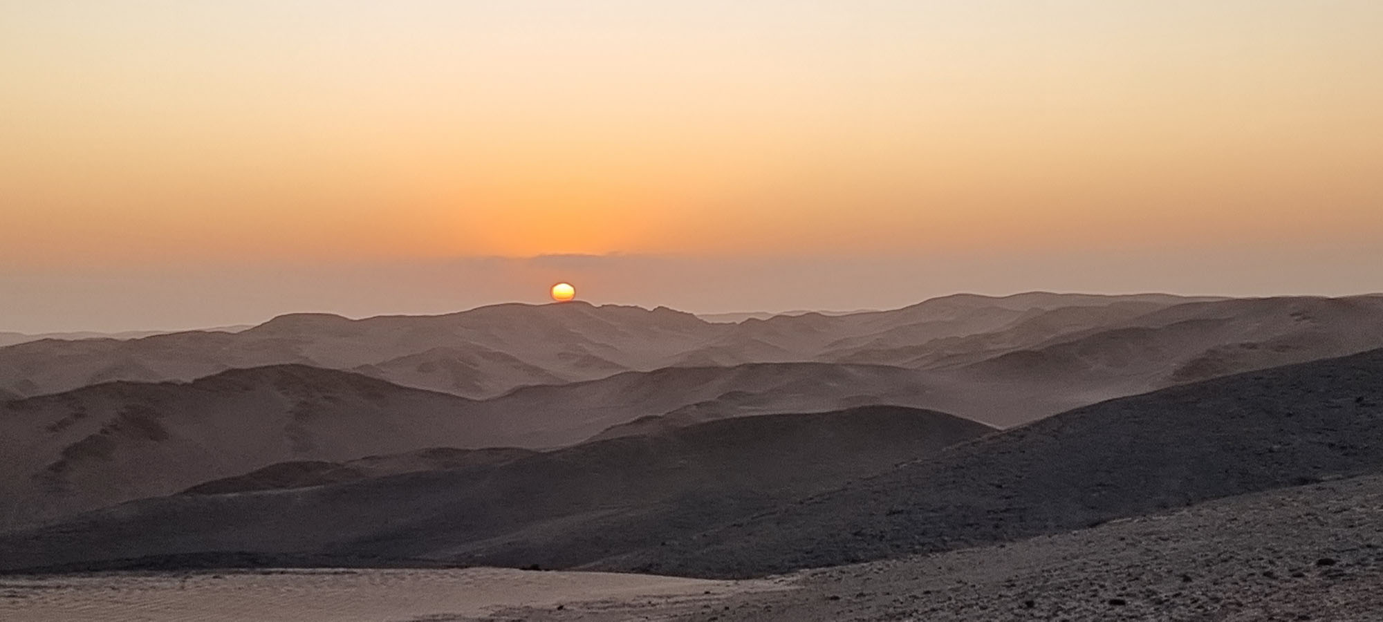 Sonnenuntergang über den kargen Dünen und Hügeln der Skeleton Coast in Namibia.