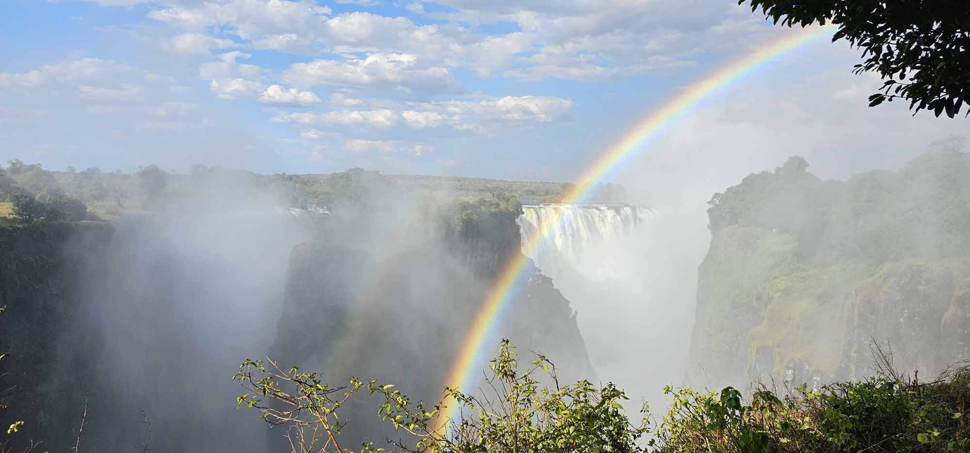 Regenbogen über den Victoriafällen an der Grenze zwischen Sambia und Simbabwe, umgeben von aufsteigendem Sprühnebel.