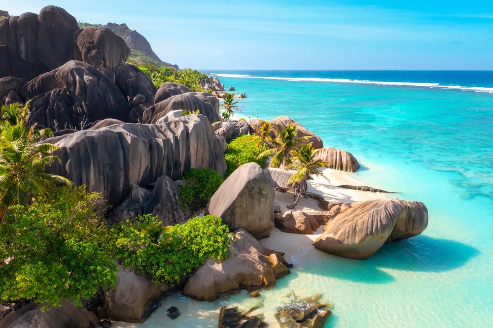 Tropische Küste der Seychellen mit markanten Granitfelsen, Palmen, weißen Sandstränden und türkisfarbenem Wasser.