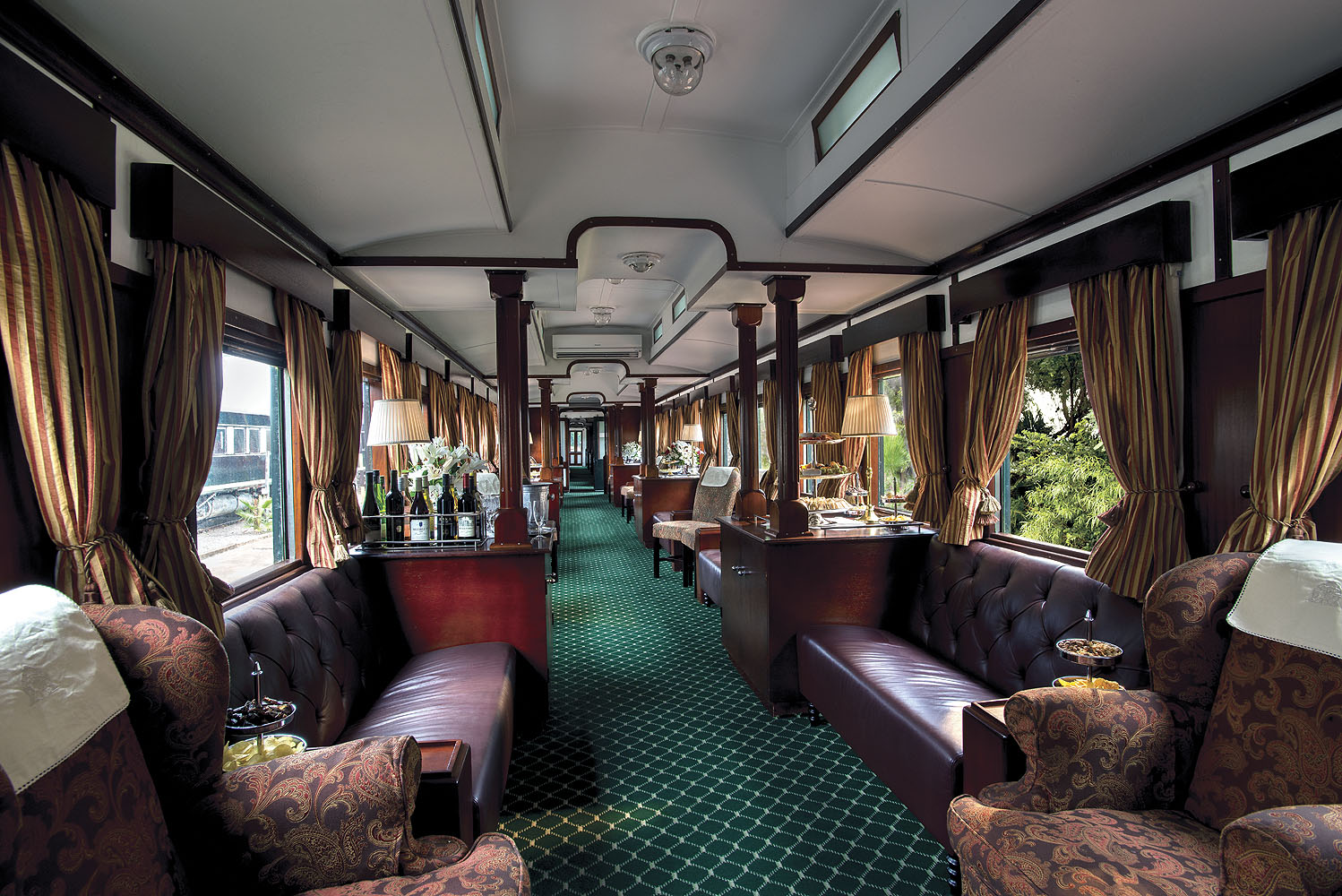 Eleganter Lounge-Wagen des Rovos Rail mit Ledersofas, klassischen Sesseln, edler Holzvertäfelung und Panoramafenstern.