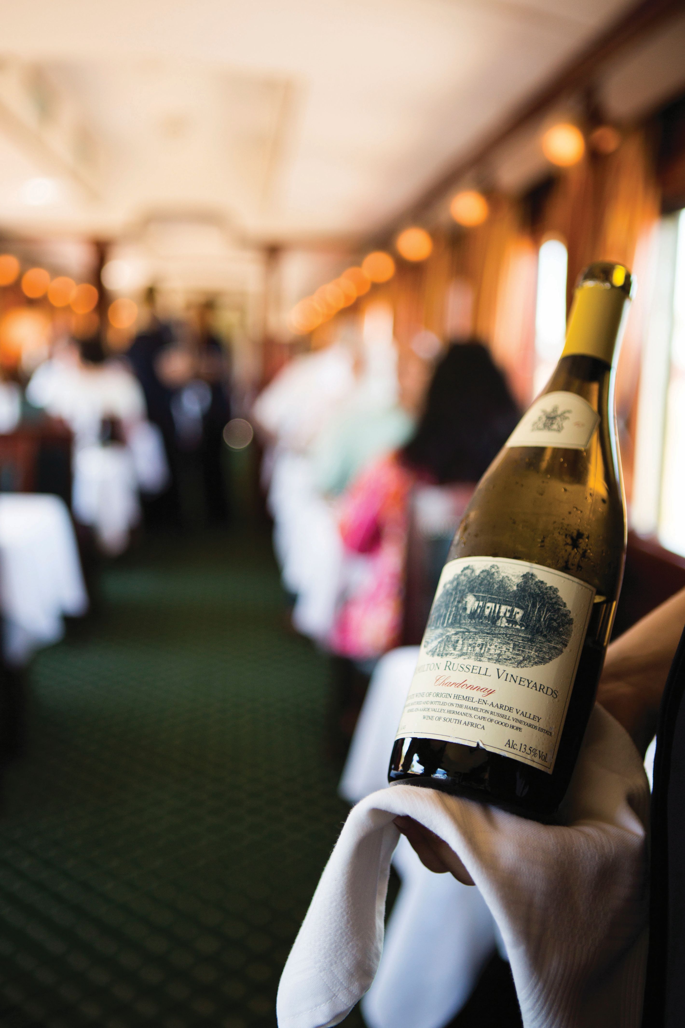 Kellner präsentiert eine Flasche südafrikanischen Weißwein im eleganten Speisewagen des Rovos Rail Luxuszuges.