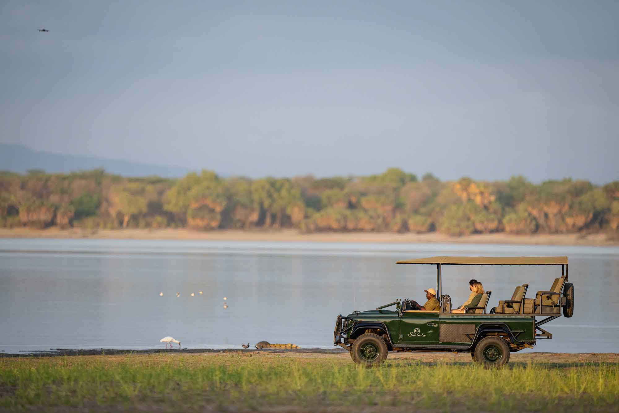 Offenes Safarifahrzeug am Ufer des Sambesi im Lower Zambezi Nationalpark in Sambia während einer Wildtierbeobachtung bei Abendlicht.