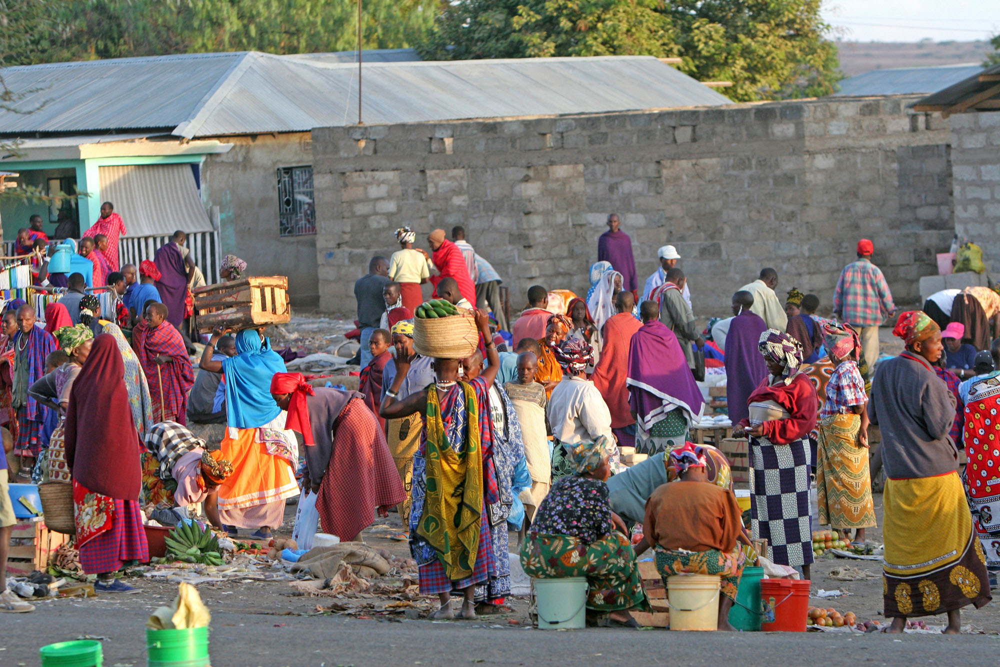 Belebter Markt in Tansania mit Einheimischen in traditioneller Kleidung, die Obst, Gemüse und Waren handeln.