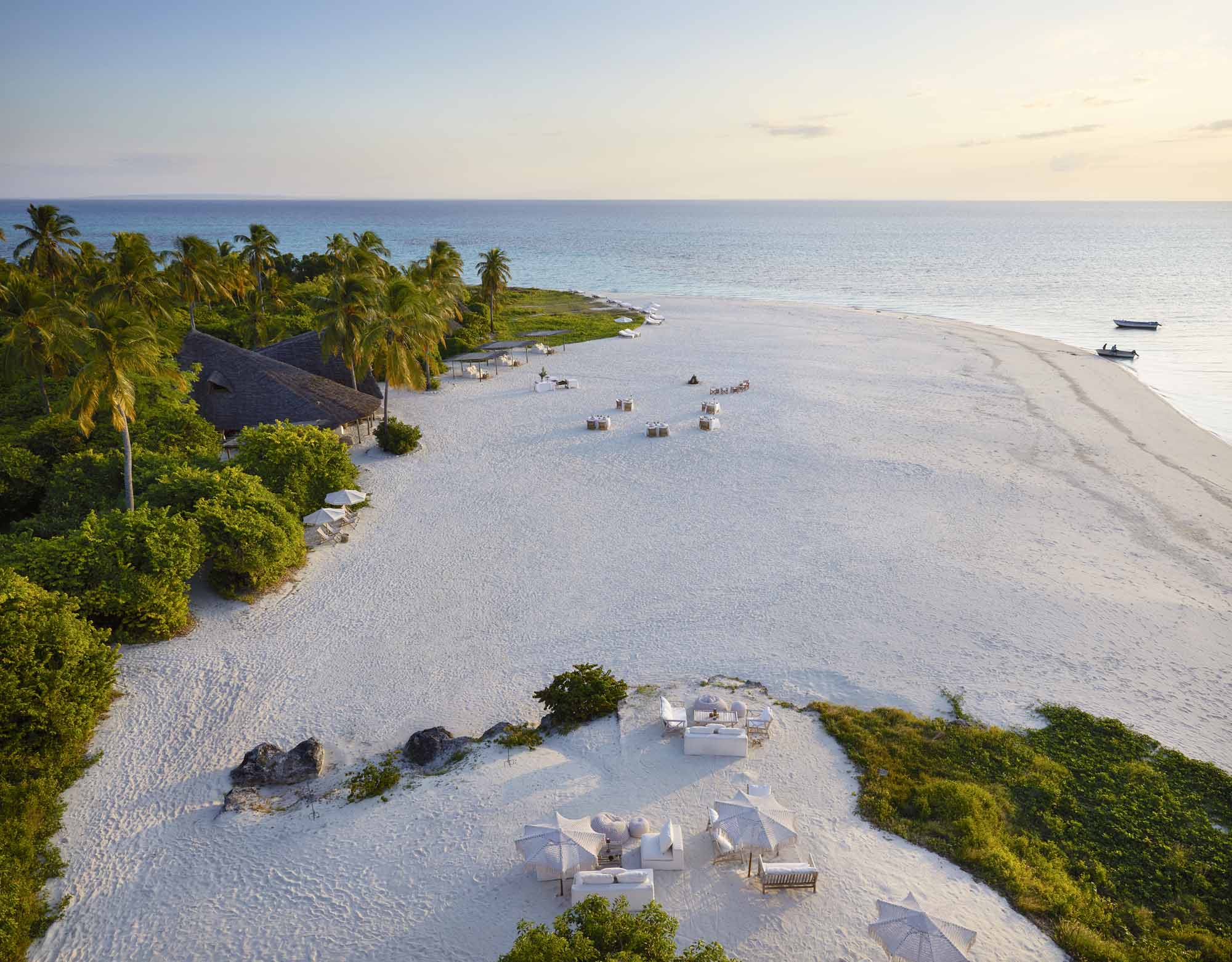 Weißer Sandstrand auf Sansibar mit Palmen, türkisblauem Meer und exklusiven Sitzbereichen direkt am Indischen Ozean.