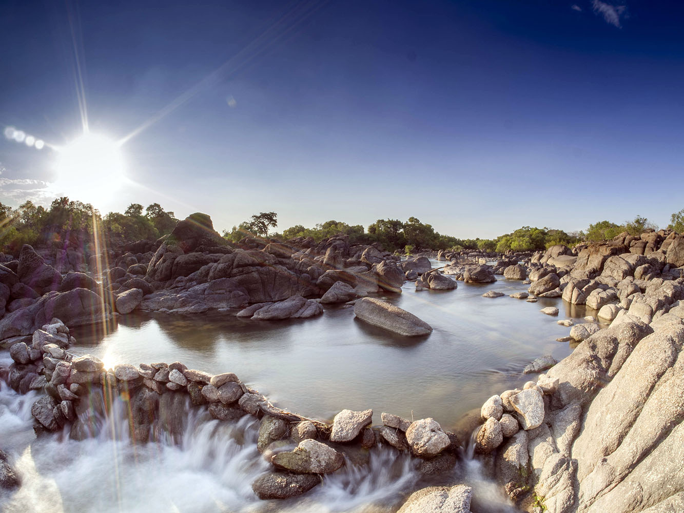 Ruhiger Fluss mit glatt geschliffenen Granitfelsen und kleinem Wasserfall in einer natürlichen Landschaft Simbabwes.
